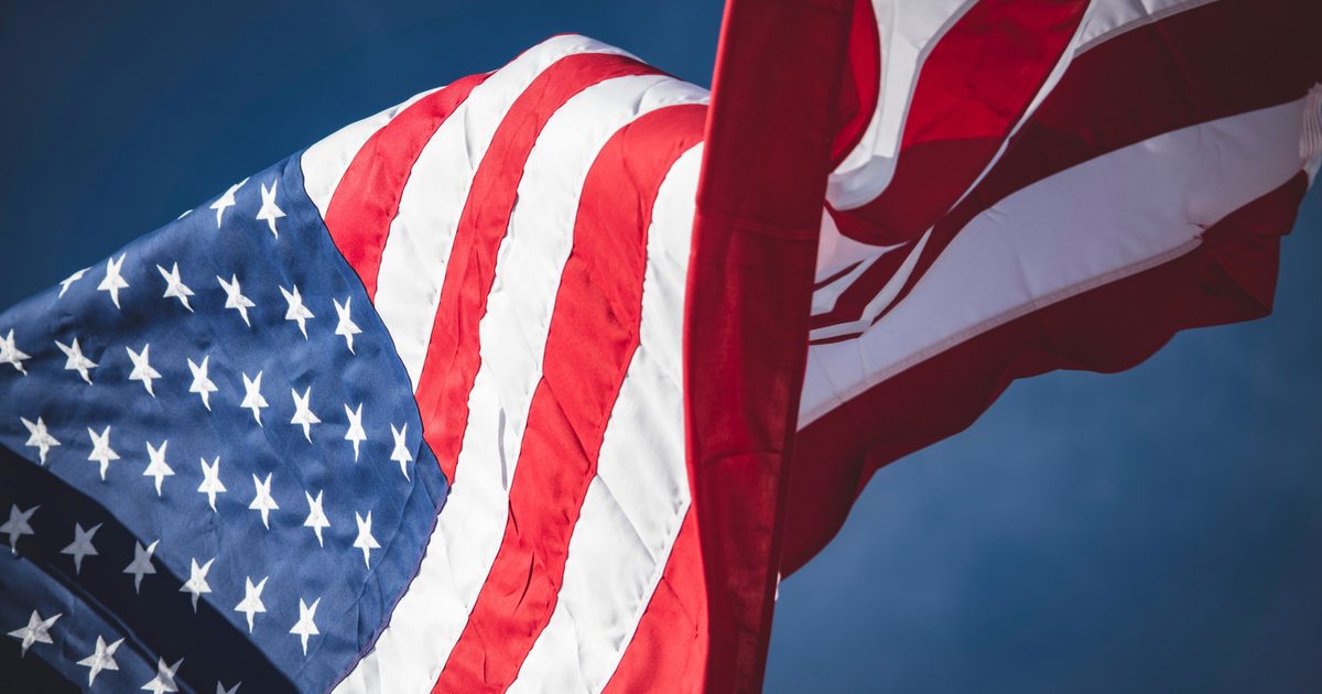 Close-up of the American flag waving against a clear blue sky, highlighting the star-spangled section and red and white stripes.