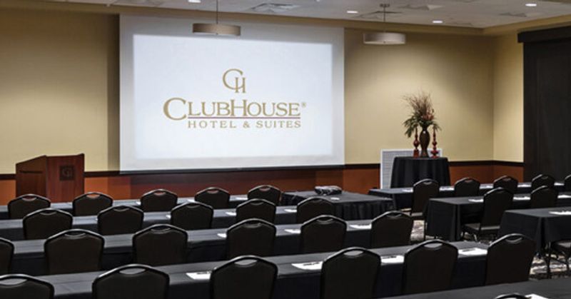 A meeting room with long tables with chairs on one side, facing a large projector with the hotel logo displayed on it.
